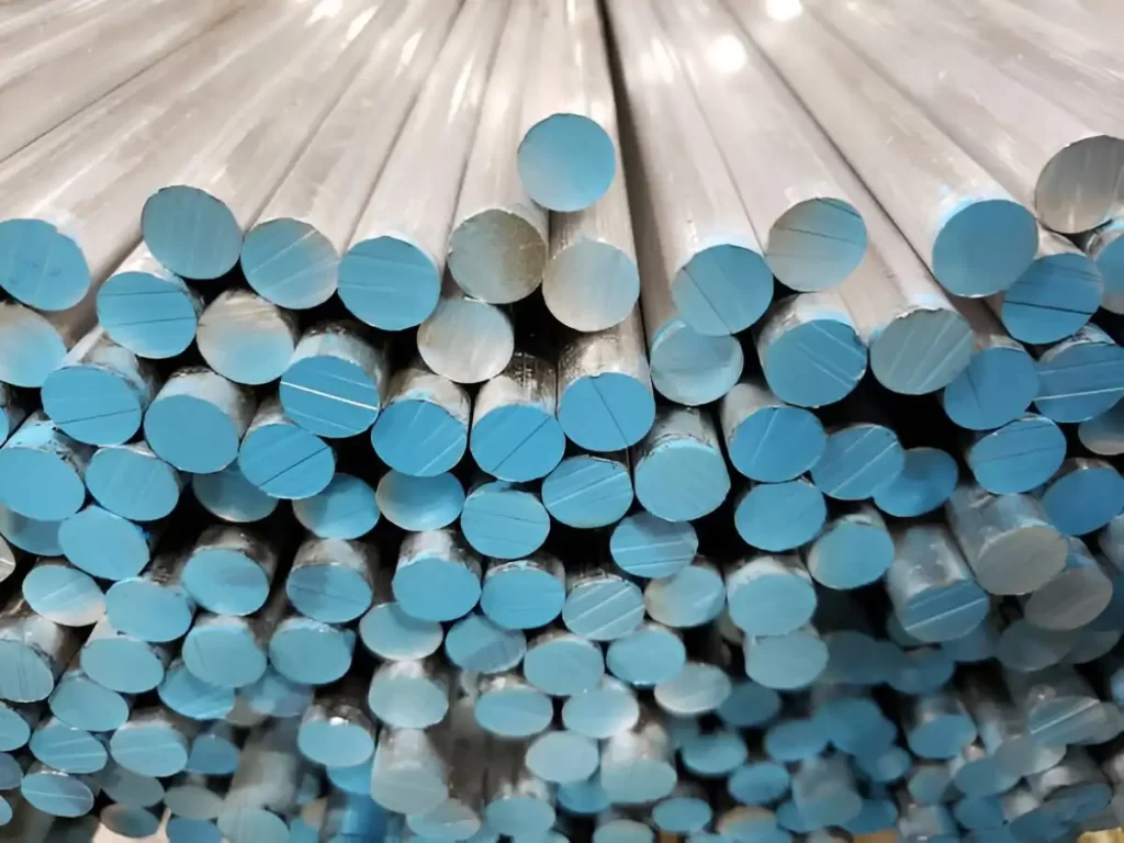 Several aluminum bar stock pieces in rectangular and round shapes, stacked in rows inside a workshop or warehouse.