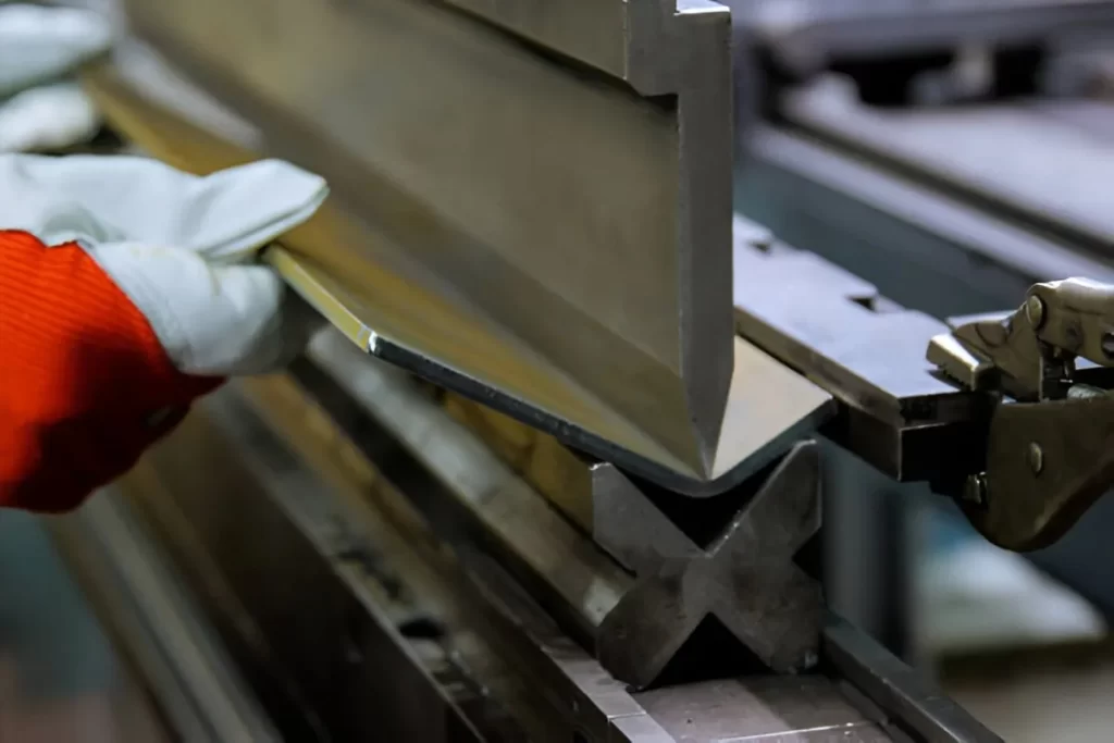 A fabricator bends a large metal plate using a press brake machine. The worker carefully aligns the sheet to ensure accurate angles during the bending process.