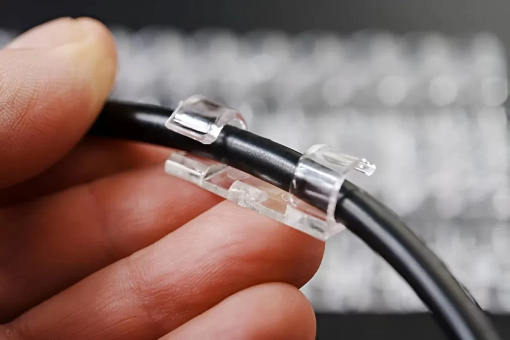 A man holds a clear acrylic wire holder next to a wire. The part is transparent and shaped to keep the wire in place.