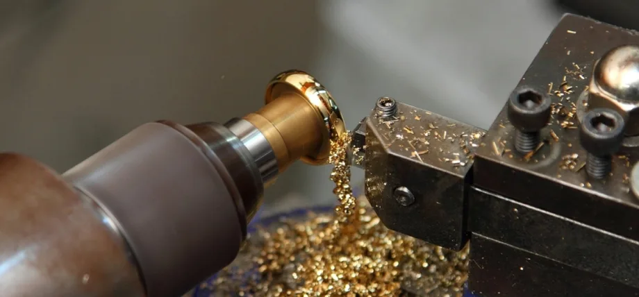 CNC lathe turning a gold ring, producing fine metal shavings as the tool shapes the workpiece.