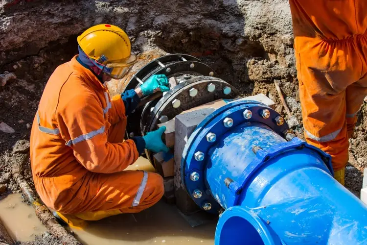 Workers installing corrosion-resistant coated pipeline with protective blue epoxy finish and stainless steel flanges