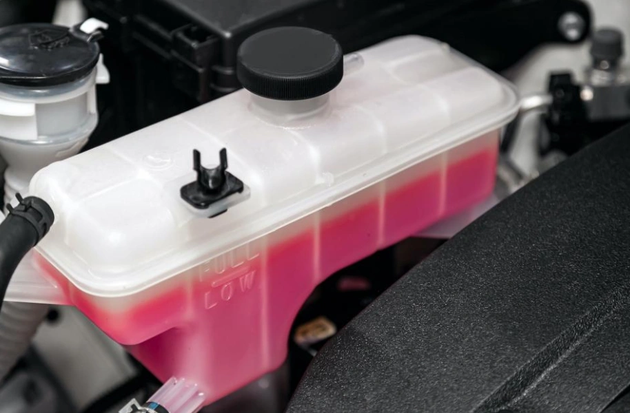 Engine coolant reservoir tank filled with pink antifreeze fluid