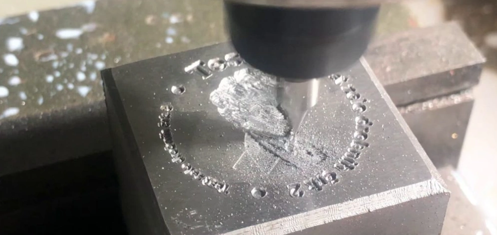 An image of an ongoing engraving process showing a portrait and text emerging on a metal block
