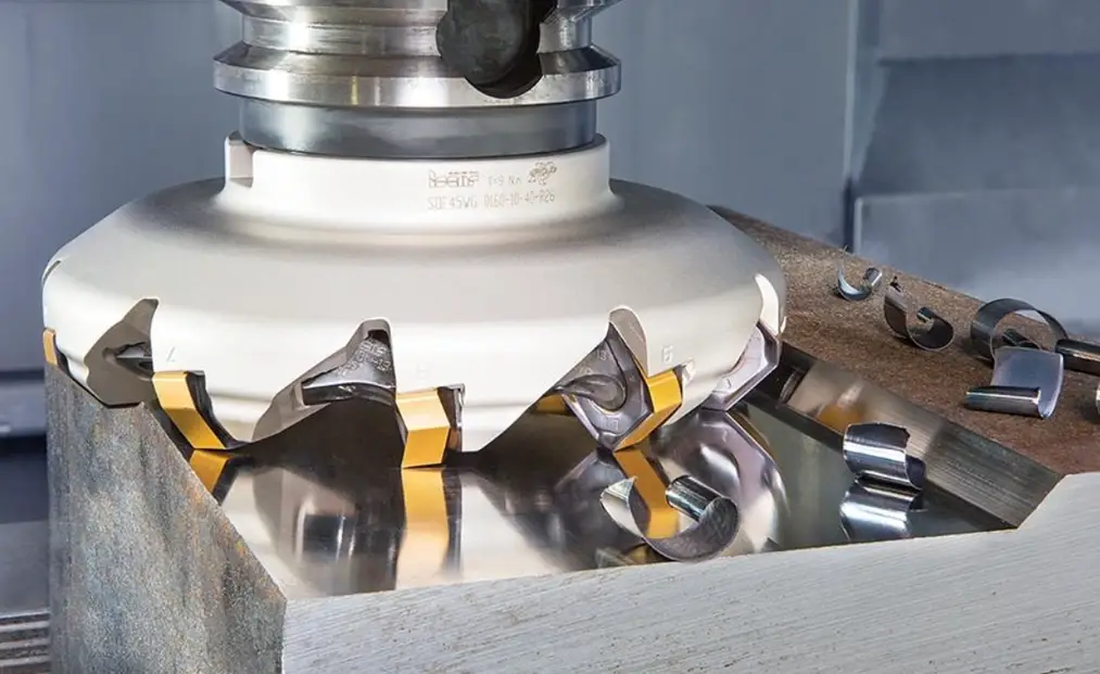 A closeup image of face milling showing a cutter with carbide inserts removing chips from a metal block 