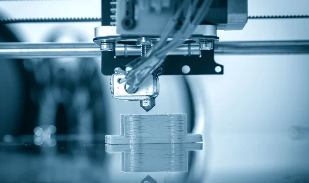 Close-up of FDM 3D printer extruder head printing layered plastic prototype part on the build platform