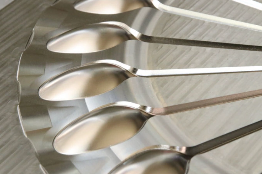 An image of a polished metal mold insert showing smooth, shiny surface cavities for plastic spoon production