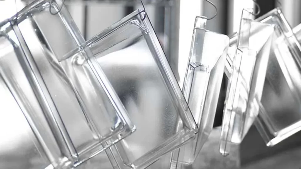 Clear plastic containers hanging on hooks, possibly after a coating process.