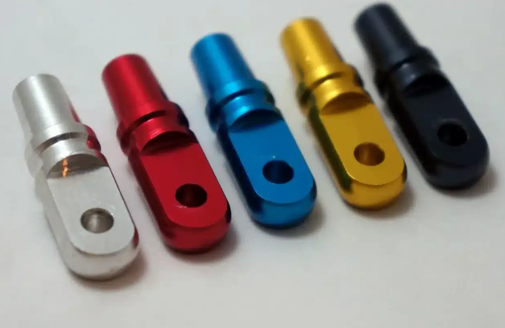 Five anodized aluminum machined components in different colors - silver, red, blue, gold, and black - with precision drilled holes demonstrating secondary finishing
