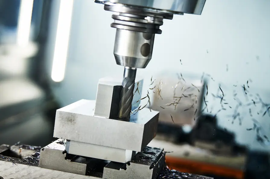 CNC milling machine cutting a metal block with a rotating end mill tool, producing sharp metal shavings during the soulder milling process.