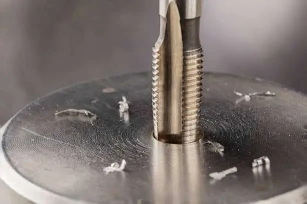 Close-up of a tap tool cutting threads into a metal hole. 